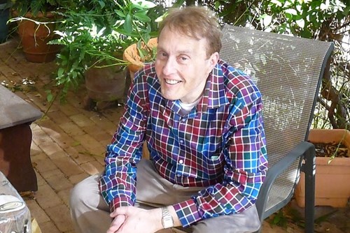 Tim, wearing a checkered shirt, sitting and smiling at the camera. 