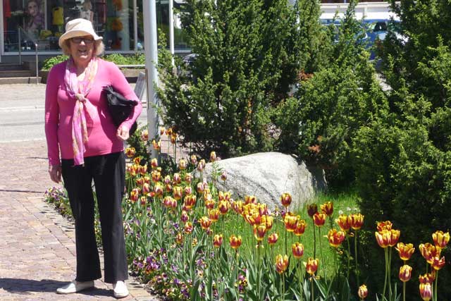 Judith, a woman wearing a pink top, standing next to a garden of flowers. 