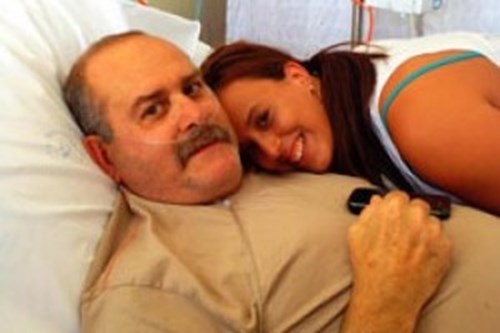 Katrina smiling next to her dad who is laying in a hospital bed. 