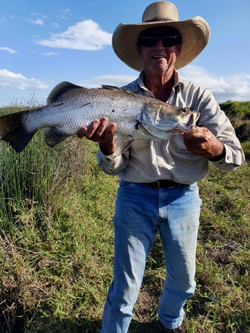 Greg wearing a cowboy hat, holding a freshly caught fish. 