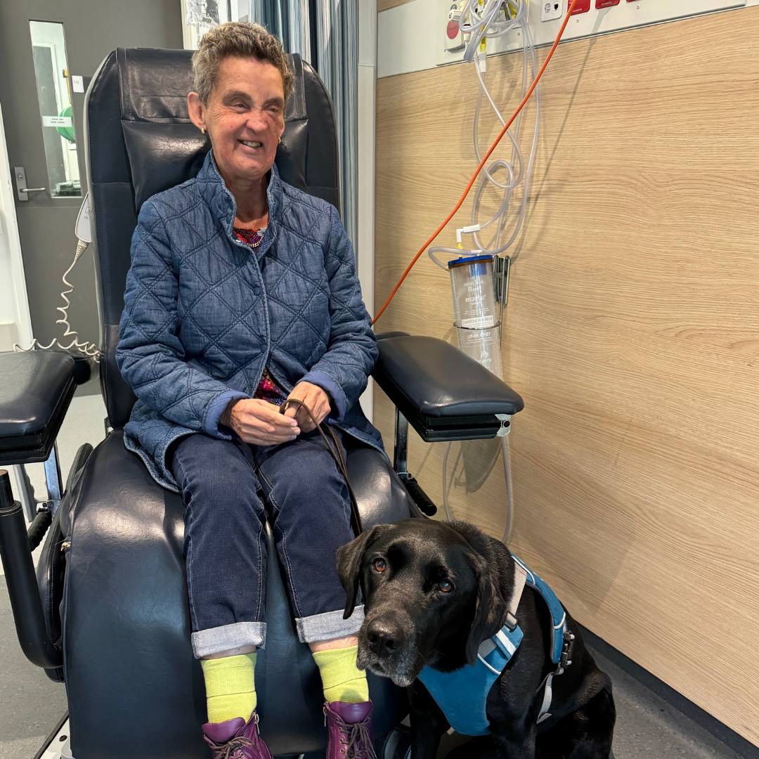 Leanne sitting on a hospital chair with 'Ester' her guide dog by her side. 