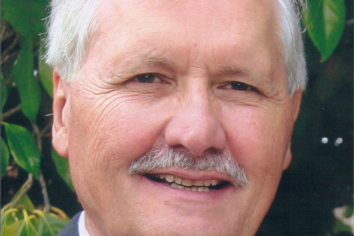Nicholas, Vassie's father, smiling in front of a garden. 