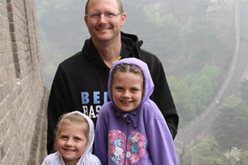 Ryan standing with his two daughters. He wears a black hoodie and the girls are wearing purple hoodies.